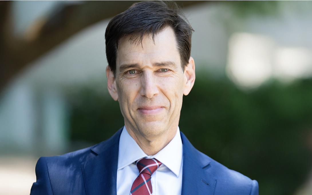 Headshot of Ted Gayer wearing a blue suit with a red striped tie